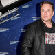 Elon Musk standing in front of a blue background near a rocket ship model.